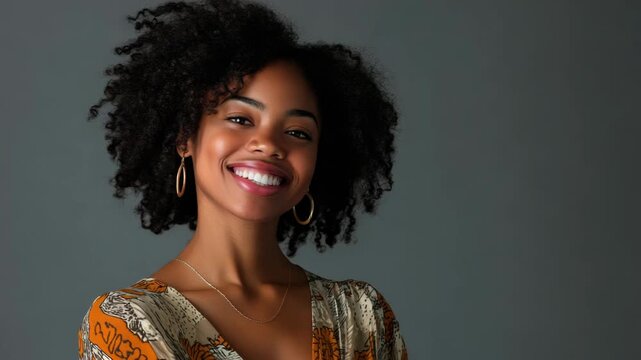 Smiling woman with natural curly hair, wearing earrings and patterned top against neutral backdrop.