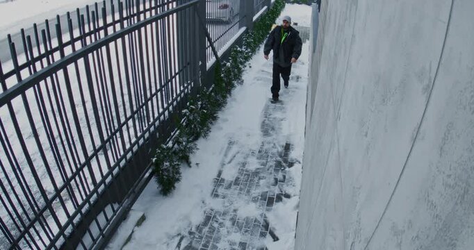 Courier From Delivery Service Moves Down Snow Cleared Sidewalk With Oversized Yellow Insulated Backpack. Winter Deliveries, Urban Logistics, And Reliable Doorstep Service Following Maintenance Work.