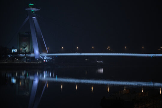 The iconic UFO bridge in Bratislava at night with reflection on the surface of the Danube - horizontal