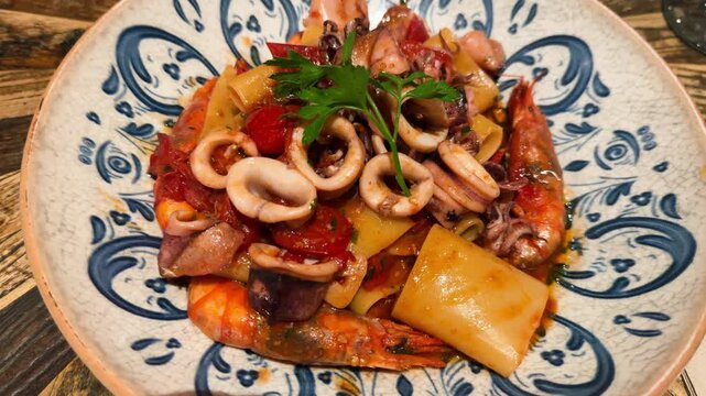 Mezzi paccheri pasta with seafood, squid, large shrimp in a tomato sauce with herbs, close-up. High quality 4k footage