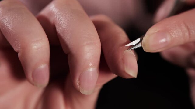 Extreme macro close up of woman trimming cuticles with manicure scissors. Precise nail care process, sharp focus on blade and fingertip, shallow depth of field and warm indoor lighting.