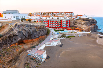 Cliffside view of Playa San Borondon, Gran Canaria, with terraced buildings, sandy beach and Atlantic Ocean under soft evening light. Coastal scene ideal for travel and architecture themes