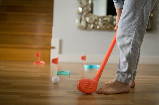  Detailed shot of a child's hands gripping an orange plastic toy golf club, practicing sports techniques in a domestic setting.