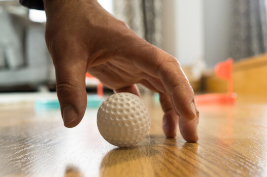 Close up of a man's hand about to pick up or place a small plastic golf ball during an indoor game.