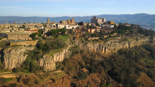 Aerial view of Orvieto old town on tuff cliff above misty valley. Medieval city silhouette in golden sunrise sunlight, fog over Umbria landscape, Italy. 4K 10-bit HDR cinematic drone footage.