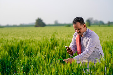 young indian farmer using smartphone standing at green wheat field © Niks Ads