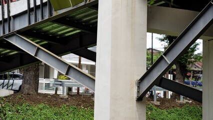 Fototapeta premium Close-up of steel beams and concrete pillars supporting a modern pedestrian overpass. An industrial architectural detail showing urban infrastructure and structural engineering.