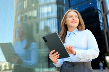 Business professional stands outside a modern building with a tablet in hand and smiles