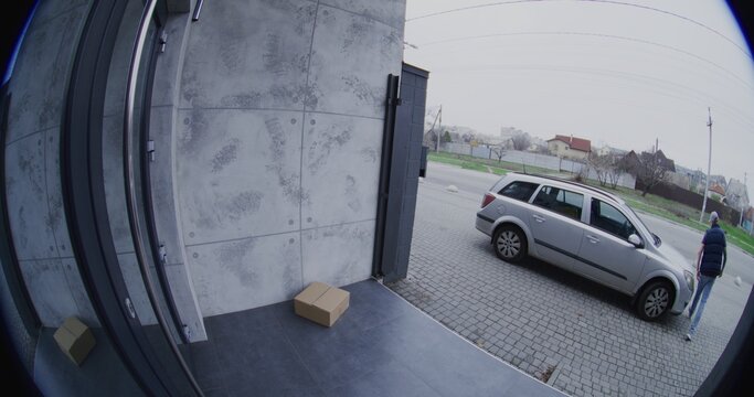 Man Pulls Up in Silver Car. Courier Retrieves Large Parcel, and Carelessly Throws it Onto Porch. Negligent Delivery Captured by Smart Doorbell Camera. Concept of Poor Service and Property Security.