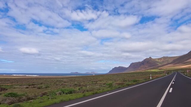 K&uuml;stenstra&szlig;e auf Lanzarote durch eine gr&uuml;n bewachsene felsige vulkanische Landschaft mit Meer und blauem Himmel am Horizont, Freiheit,  Erkundung, reisen, Roadtrip, Kanarische Inseln, Spanien