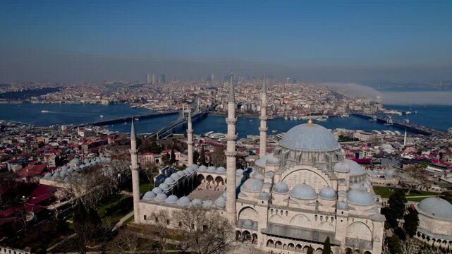 Aerial drone view of S&uuml;leymaniye Mosque in Istanbul, featuring its domes and minarets with the Golden Horn, bridges, boats and historic city skyline in the background.