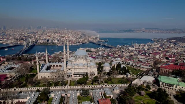 Aerial drone view of S&uuml;leymaniye Mosque in Istanbul, featuring its domes and minarets with the Golden Horn, bridges, boats and historic city skyline in the background.