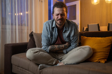 Fototapeta premium Man experiencing abdominal pain while relaxing on sofa at home