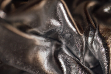 Obraz premium Close-up of crumpled black fabric with a shiny texture, showcasing intricate details and reflections under soft lighting, ideal for textile and fashion design applications