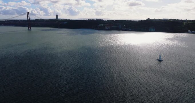 High altitude drone shot drifting over Lisbon metropolitan area toward the river with layered neighborhoods, open water and distant horizon for cinematic European city storytelling