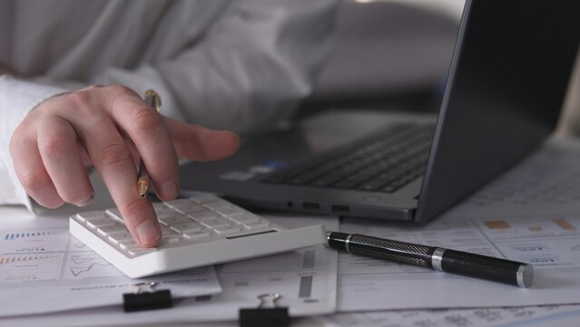 Verifying Financial Figures. Assessing Sums On Calculator Beside Laptop During Business Review. Checking Financial Totals With Calculator And Documents In Professional Setting