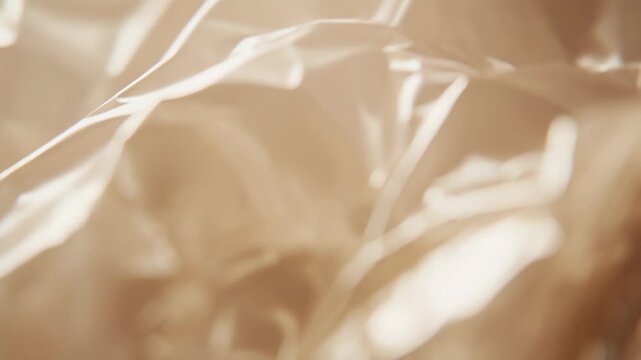 Crumpled plastic film generating abstract background texture with soft creases and reflections, highlighted by warm golden light creating a luminous, dynamic surface