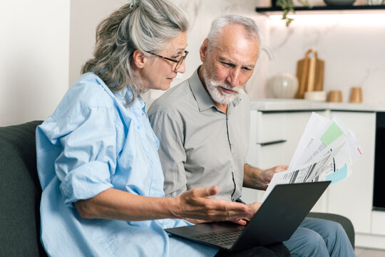 Couple discusses bills and budget while reviewing statements on laptop at home