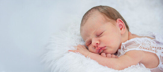 Sleeping newborn baby girl in a white lace dress and headband on a fluffy blanket.