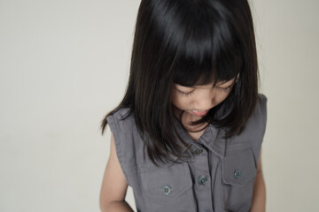 Fototapeta premium Asian little girl looking down wearing gray dress on neutral background, calm child portrait and kids fashion concept.