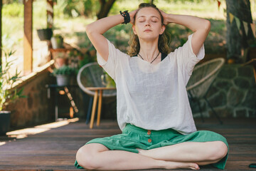 Young blonde woman practicing yoga and meditation on a sunny summer terrace.