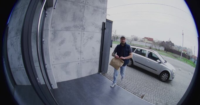 Male Courier Ringing Bell and Leaving an Order at Door. Adult Man With Tattoo in Arms Takes Photo With Smartphone For Proof of Delivery and Then Leaves. Concept of Modern Smart Home Tracking.