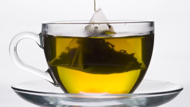 Tea in a Cup Takes on a Rich Color. A pyramid-shaped tea bag is slowly dipped into a glass mug
