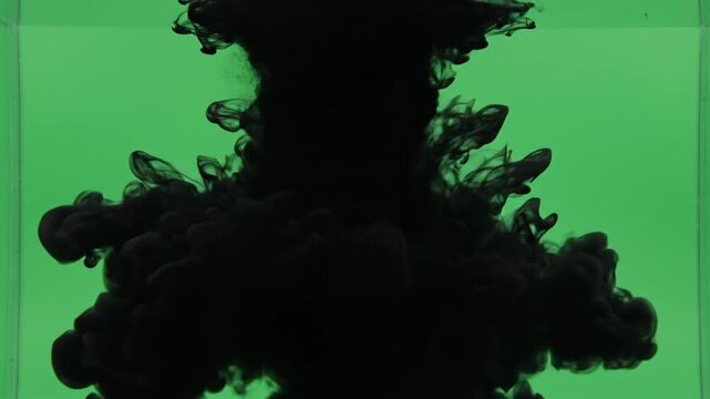 Black ink drops into clear water creating cloud shapes in a green background