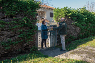 People exchange greetings and talk by a gate outside a house © Iryna