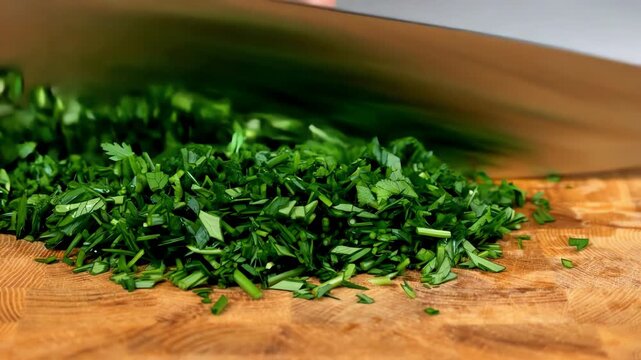 Hands of chef chopping fresh green herbs with sharp metal knife on wooden cutting board