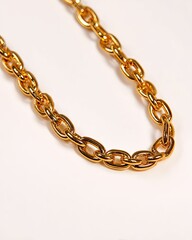 Obraz premium Close-up of a gleaming gold chain lying on a white surface, creating an elegant curve