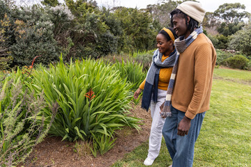 African American couple standing in park by mulch bed, with scarves, viewing red blooms, copy space