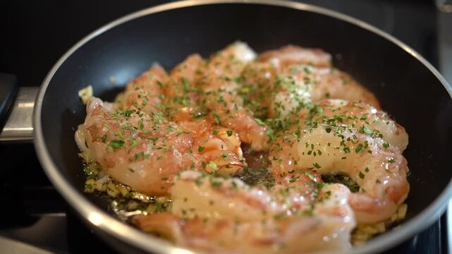 Shrimp saut ing in olive oil with garlic and parsley in a frying pan on the stove fresh, homemade seafood meal preparation