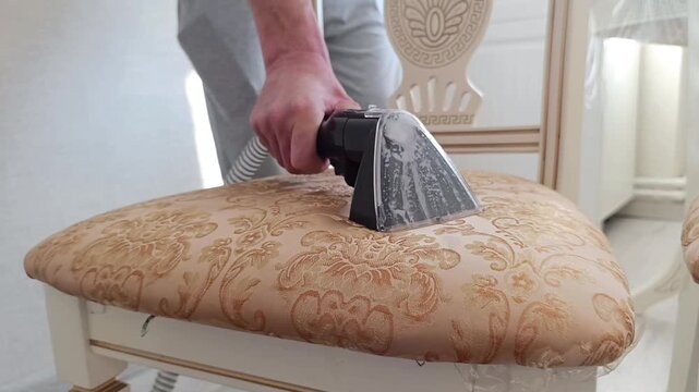 Professional upholstery steam cleaning: handheld vacuum extractor removing dirt from chair fabric