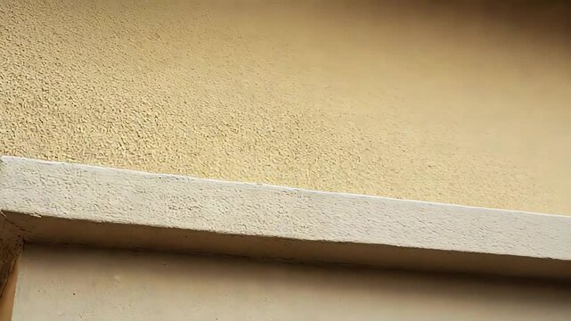 Architectural detail of a building facade with contrasting textures and shades, featuring a rough stucco wall meeting a smooth, clean corner providing an abstract and modern background