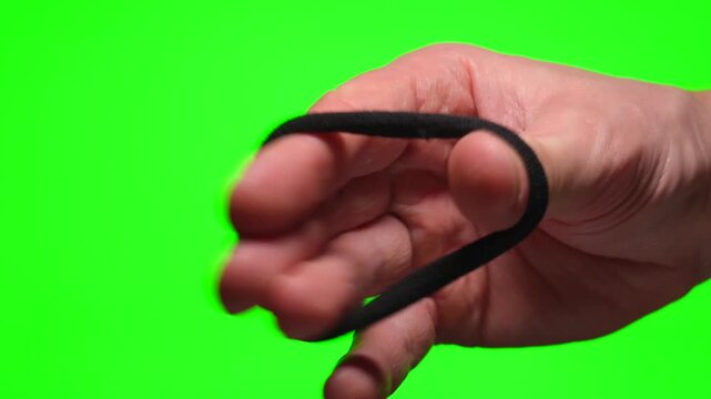 A man's hand stretches an elastic hair tie against a green background.
A black hair tie on a Chroma Key.