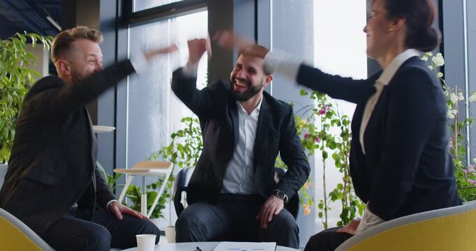 Smiling business professionals shaking and stacking hands during work meeting in office. Cheerful confident entrepreneurs finalizing deal, clapping hands and celebrating successful partnership.