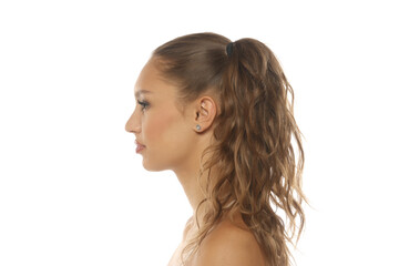 Fototapeta premium Side view portrait of a young woman with brown wavy hair in a side ponytail, studio shot on a white background