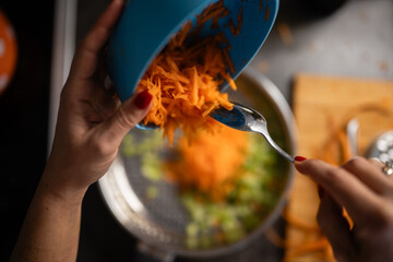 Obraz premium Hands adding shredded carrots to cooking vegetables