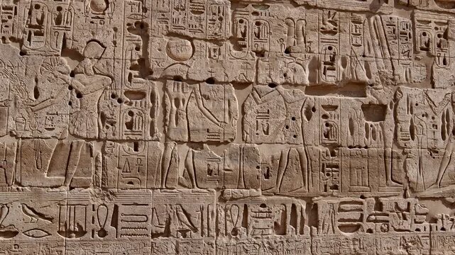 Closeup of ancient Egyptian hieroglyphic inscriptions with cartouches and bird symbols carved in sandstone wall at Medinet Habu temple in Luxor Egypt, detailed royal text.