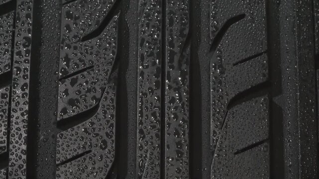 Wet Tread Car Tire Close Up. The surface of a car tire covered with shiny water drops slowly floats in front of the camera close-up