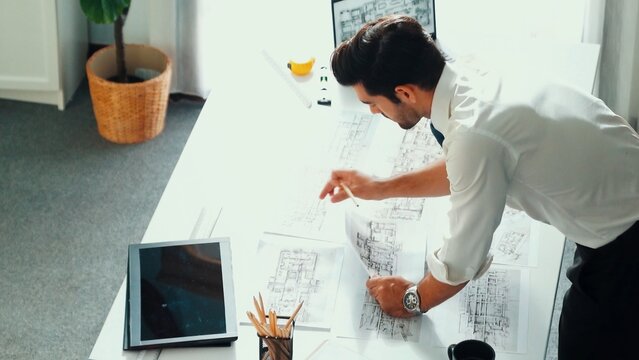 Architect engineer using laptop planning house design at office while sitting at meeting table with blueprint and equipment scatter around.Skilled civil engineer working at blueprint. Alimentation.