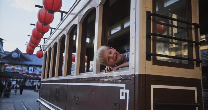 Smiling young boy peeking out of Japanese trolly window - steady cam shot