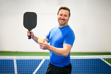 Positive men looking at camera while playing pickleball at court indoor