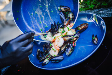 Apetyczne małże i krewetki w jasnym sosie podane na niebieskim talerzu. © Artur