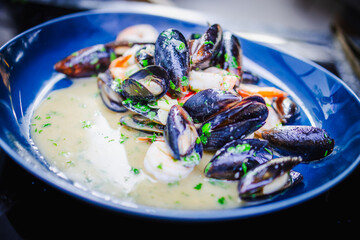Apetyczne małże i krewetki w jasnym sosie podane na niebieskim talerzu. © Artur
