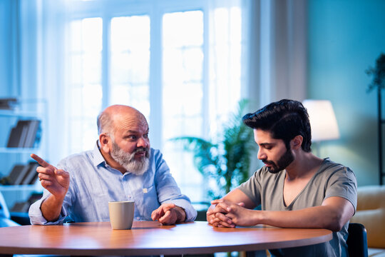 Indian Elderly dad guiding his grown son in a thoughtful family moment indoors.
