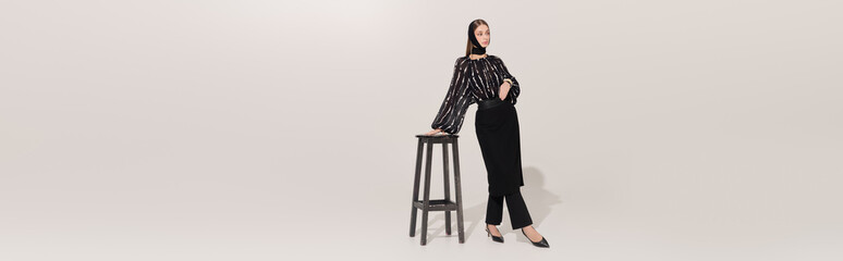 Naklejka premium Elegant young woman showcasing sophisticated fashion in a grey studio
