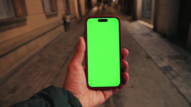 Hand holding smartphone with green screen in street at night, person walking on the street with gadget. High quality 4k footage