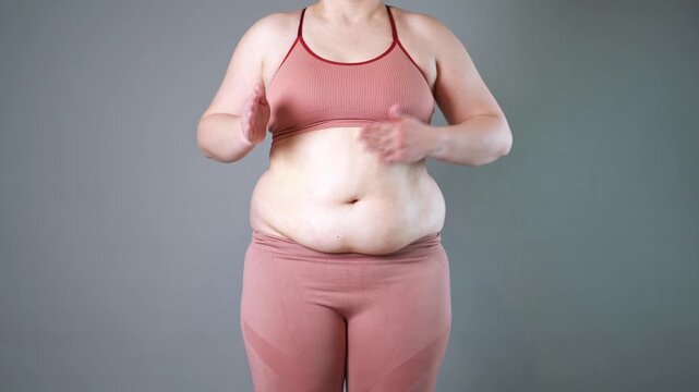 Abdominal massage, tummy tuck and flabby skin on a fat belly, woman doing self-massage with cream on gray studio background